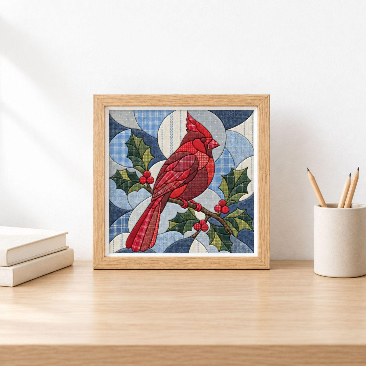 May include: A square framed wall art piece featuring a red cardinal bird perched on a holly branch with green leaves and red berries. The design uses a patchwork style with various blue and white plaid patterns forming a circular background.