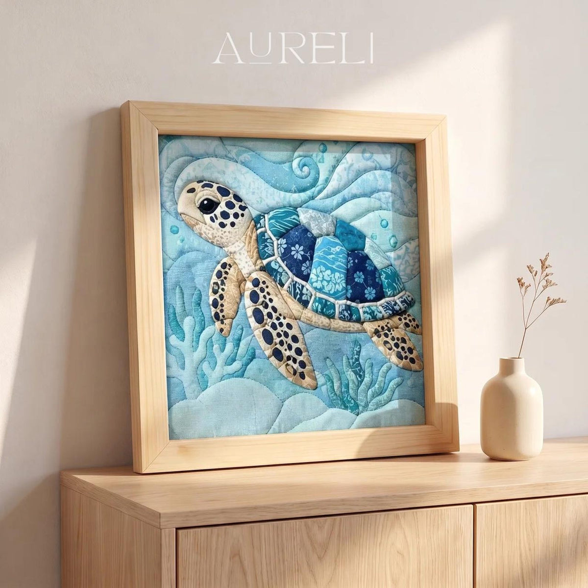 May include: A square framed textile art piece featuring a sea turtle swimming through blue waves and coral. The turtle has a patterned shell in shades of blue and white. The word AURELI is printed in white at the top center of the frame.