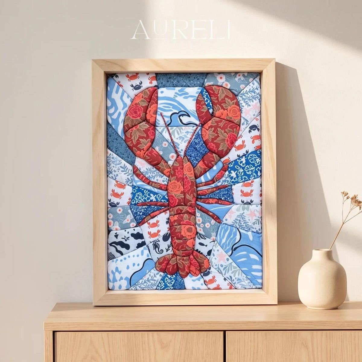 May include: A rectangular framed fabric wall art piece featuring a central red lobster motif constructed from floral patterned fabric. The background consists of various blue and white patterned fabric segments with small crab and wave illustrations.