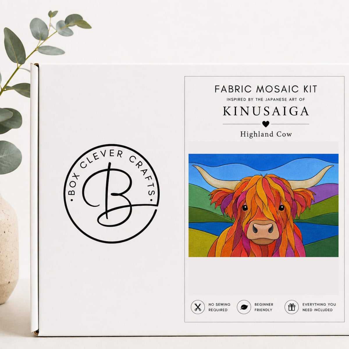 May include: A white rectangular box for a fabric mosaic kit featuring the Box Clever Crafts logo and text reading Fabric Mosaic Kit, Inspired by the Japanese Art of Kinusaiga, Highland Cow. The box displays a colorful illustration of a cow.
