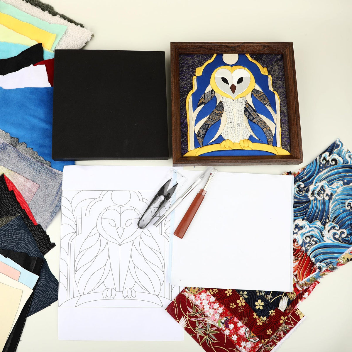 May include: A craft kit featuring a finished framed owl fabric mosaic, a black foam board, a printed owl line art pattern, a pair of small scissors, a metal stylus, and various colorful fabric swatches including blue wave and floral patterns.
