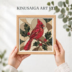 May include: A Kinusaiga art kit featuring a square wooden frame containing a fabric collage of a red cardinal bird perched on a branch with green holly leaves and red berries. The background consists of geometric shapes in beige and brown plaid.