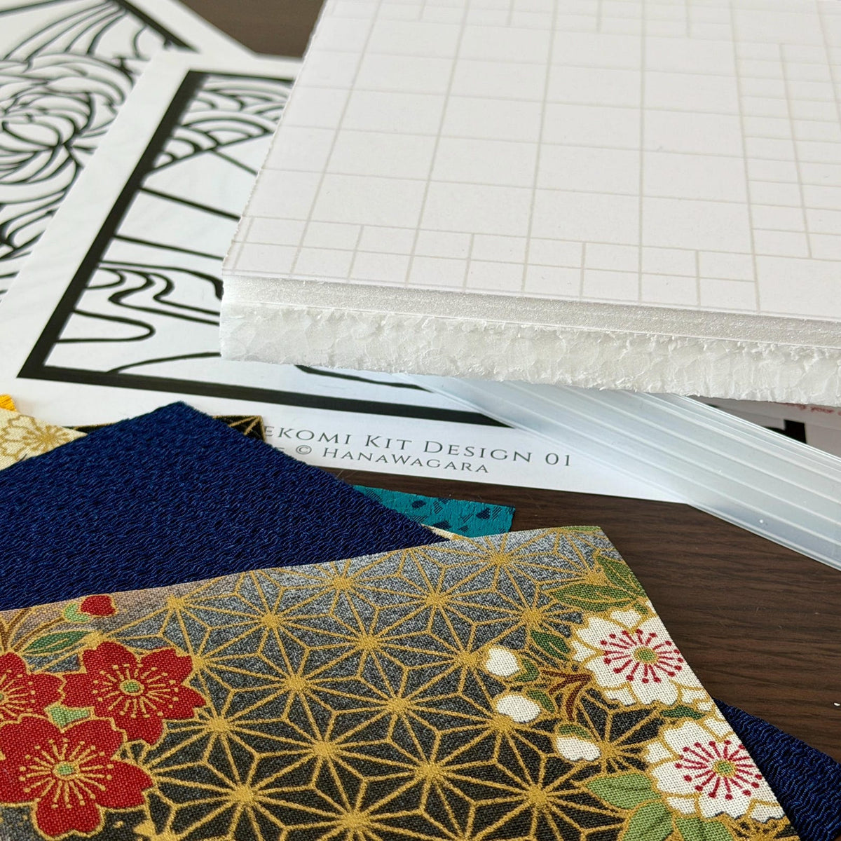 May include: A craft kit labeled KIMEKOMI KIT DESIGN 01 HANAWAGARA featuring a white foam board with a grid pattern, black and white line art templates, and several fabric swatches including a dark blue textured piece and a floral print.