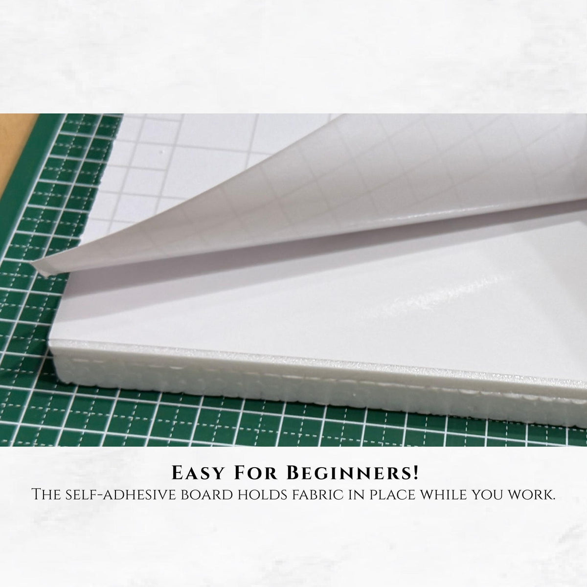 May include: A white self-adhesive board with a grid-patterned backing paper partially peeled back to reveal the sticky surface. The text below reads: EASY FOR BEGINNERS! THE SELF-ADHESIVE BOARD HOLDS FABRIC IN PLACE WHILE YOU WORK.