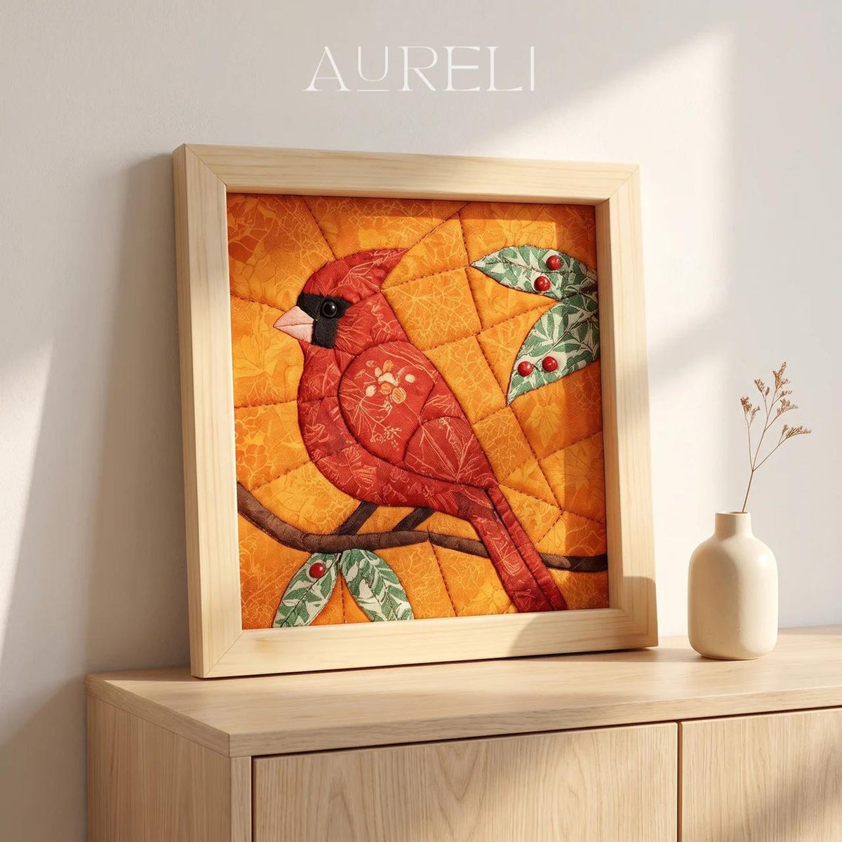 May include: A square framed fabric wall art piece featuring a quilted cardinal bird in shades of red, perched on a brown branch against an orange background. The design includes green leaves with small red berries and the text AURELI at the top.